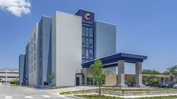 A modern hotel with a prominent blue and white facade, a covered entrance, and a parking area with cars.