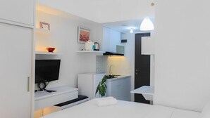 A compact, modern room with a bed, a small kitchenette, and a TV. - Serpong Garden Apartment by Kakarama (Cisauk)