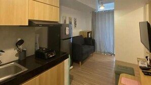 A compact kitchen with wooden cabinets, a black countertop, and a built-in oven. There is a small seating area with a dark sofa and a television. - Serpong Garden Apartment by Kakarama (Cisauk)