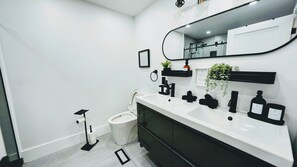 A modern bathroom with a white sink, black cabinet, and a large mirror. There are black toiletries and a small plant on the counter. - Newly Renovated Secluded Cottage (Huntsville)