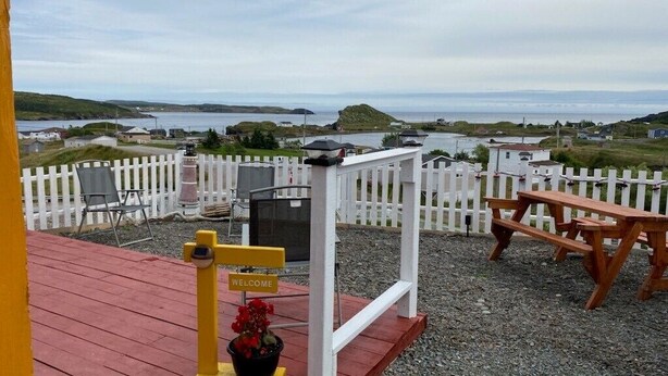 Une terrasse agrémentée d’une pancarte de bienvenue, d’un banc et offrant une vue sur la mer et les collines.