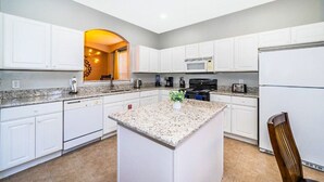 A modern kitchen with white cabinetry, granite countertops, a central island, and a built-in microwave. - 8 Bedroom home with pool, spa & games room near Disney (Kissimmee)