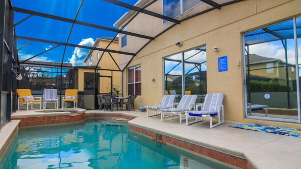 An indoor pool area with lounge chairs and a glass enclosure. - 8 Bedroom home with pool, spa & games room near Disney (Kissimmee)