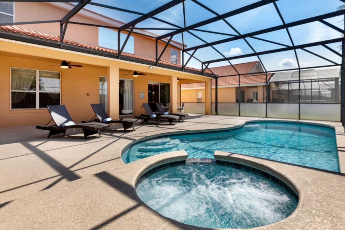 A swimming pool with lounge chairs and a hot tub, surrounded by a covered patio area.