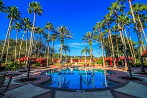 A swimming pool surrounded by tall palm trees and red structures, likely part of a resort.
