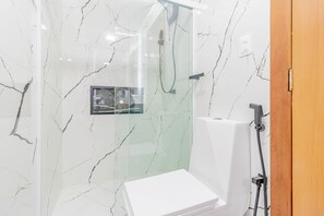 Un baño moderno con cabina de ducha de vidrio, inodoro blanco y pared con diseño de mármol.