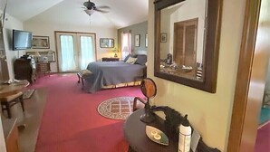 A bedroom with a bed, a desk, a chair, a mirror, and a ceiling fan.