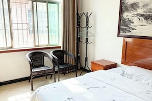 A hotel room with a bed, two chairs, a coat rack, and a window with curtains. - Jinxiang Hotel (Zhangjiajie)