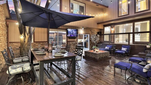 An outdoor patio with a wooden deck, a dining table set with plates and glasses, and a large umbrella.