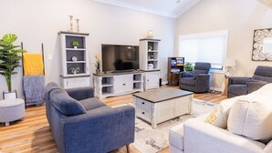 A modern living room with grey sofas, a flat-screen TV, white shelving units, and a wooden coffee table.