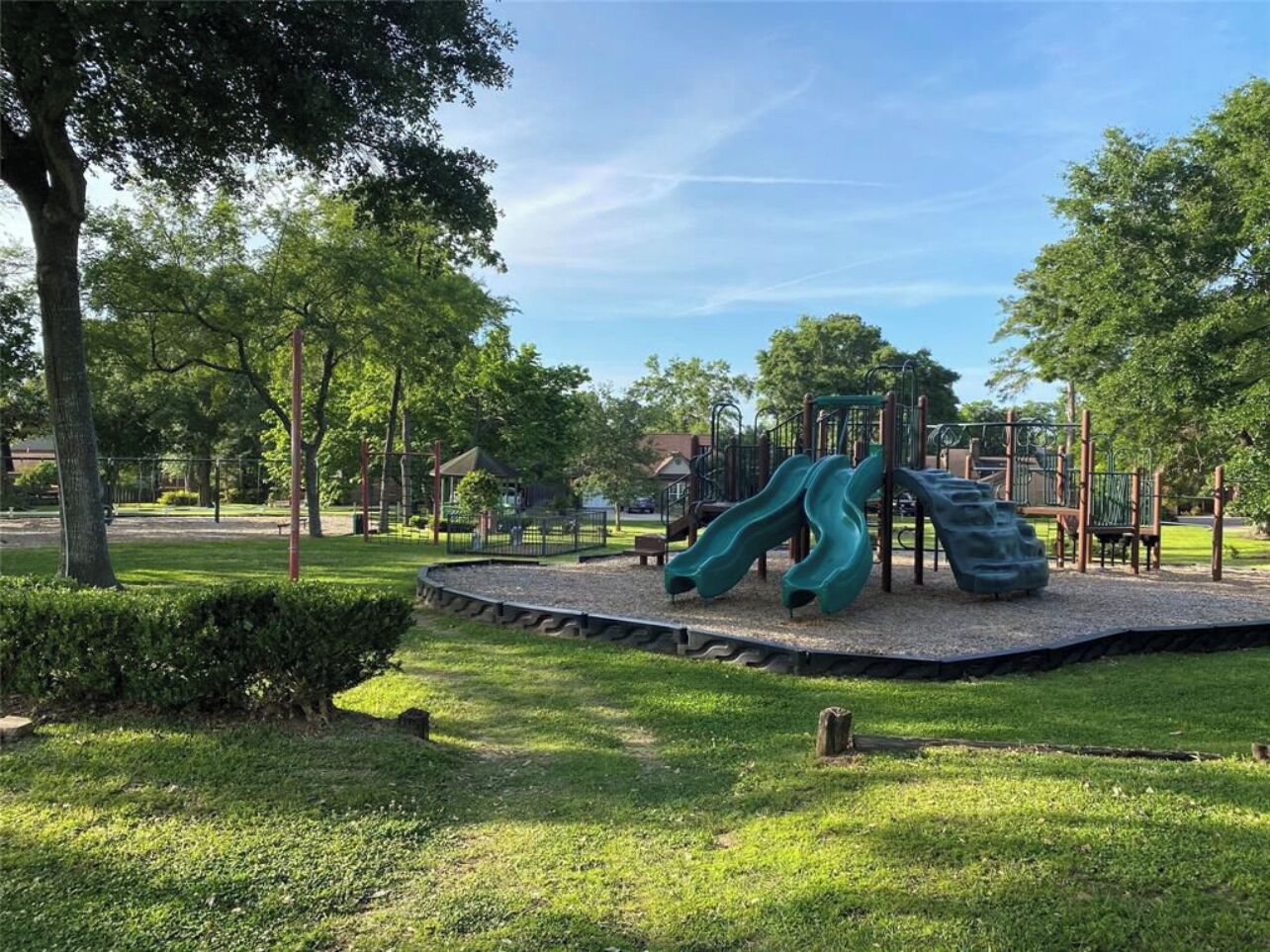 A playground with two slides and a climbing structure, surrounded by trees and grass.