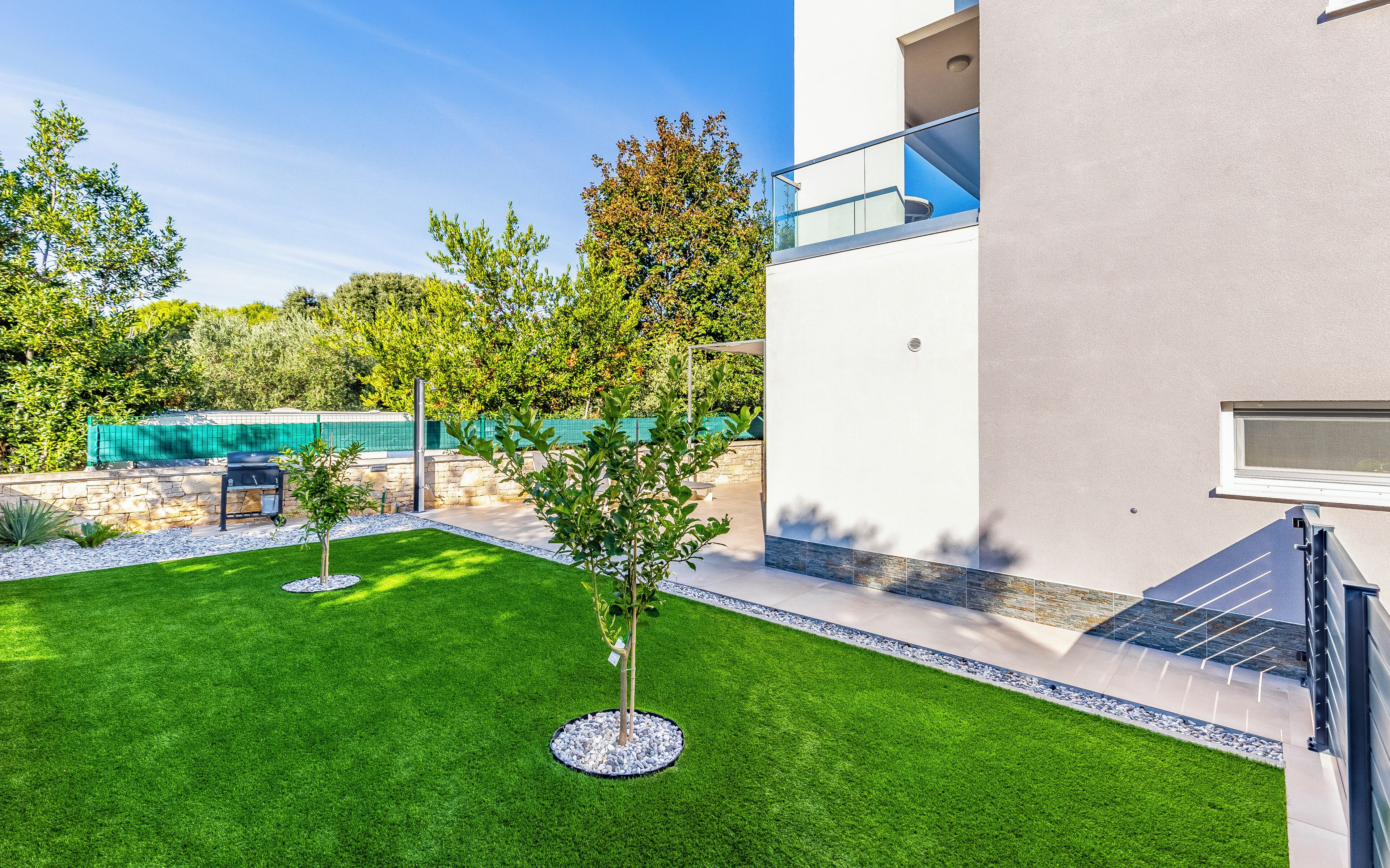 A modern house with a well-maintained lawn, a barbecue area, and a stone wall.