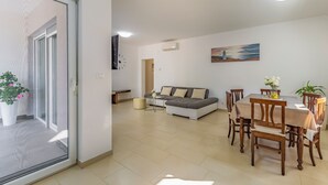 Una sala de estar moderna con sofá, mesa de comedor y sillas. Hay un cuadro en la pared y un reloj.