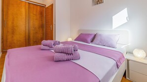 Un dormitorio con cama, ropa de cama morada, un armario de madera y una mesita de noche con una lámpara.