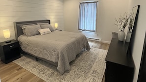 A modern bedroom with a bed, bedside tables, a nightstand, a dresser, a window with curtains, and a mirror. - Brand new, modern, cozy house in the woods! (Greig)