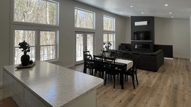 A modern kitchen with a marble countertop, dining area with chairs, and a built-in oven. - Brand new, modern, cozy house in the woods! (Greig)