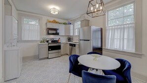 Una cocina moderna con armarios blancos, un refrigerador de acero inoxidable y un comedor con una mesa redonda y sillas azules.