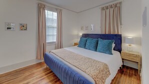Un dormitorio con una cama grande, una mesita de noche, una ventana con cortinas y cuadros en la pared.