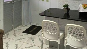 A kitchen with white tiles, a black countertop, two white chairs, and a small potted plant. - 1 Family and cozy apartment (Maragogi)