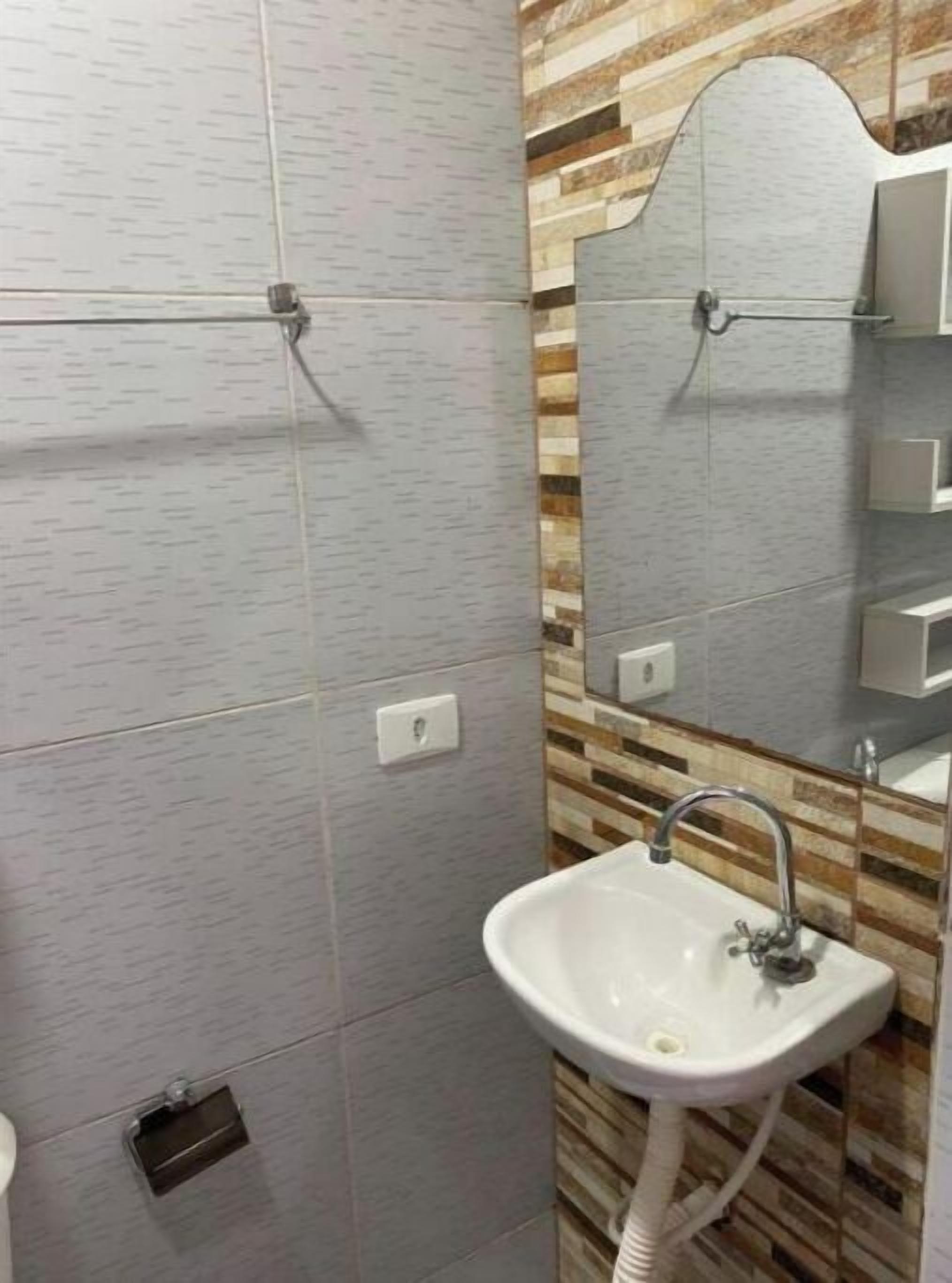 A bathroom with a white sink, a mirror, and a tiled wall.
