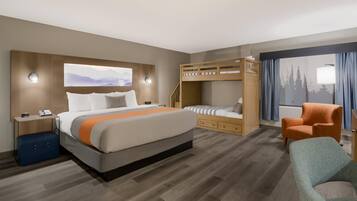 Una habitación de hotel con una cama grande, una cama individual superpuesta, un escritorio con lámpara, una silla y una ventana con cortinas.