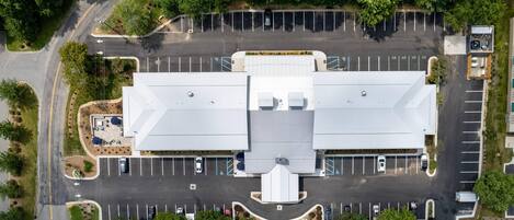 An aerial view of a parking lot with a large building in the center, surrounded by trees and a curved road.