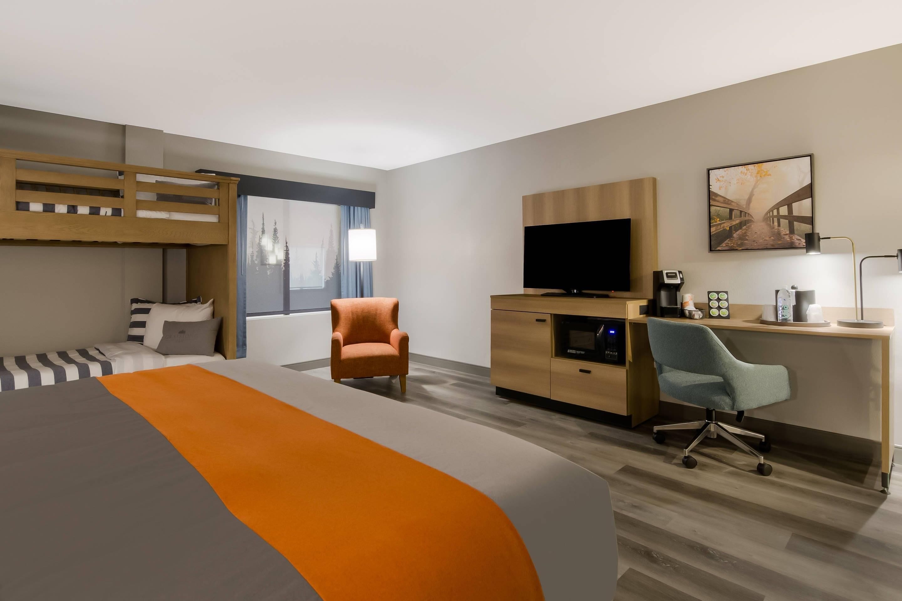 A hotel room with a bed, a desk, a chair, a TV, and a painting on the wall.