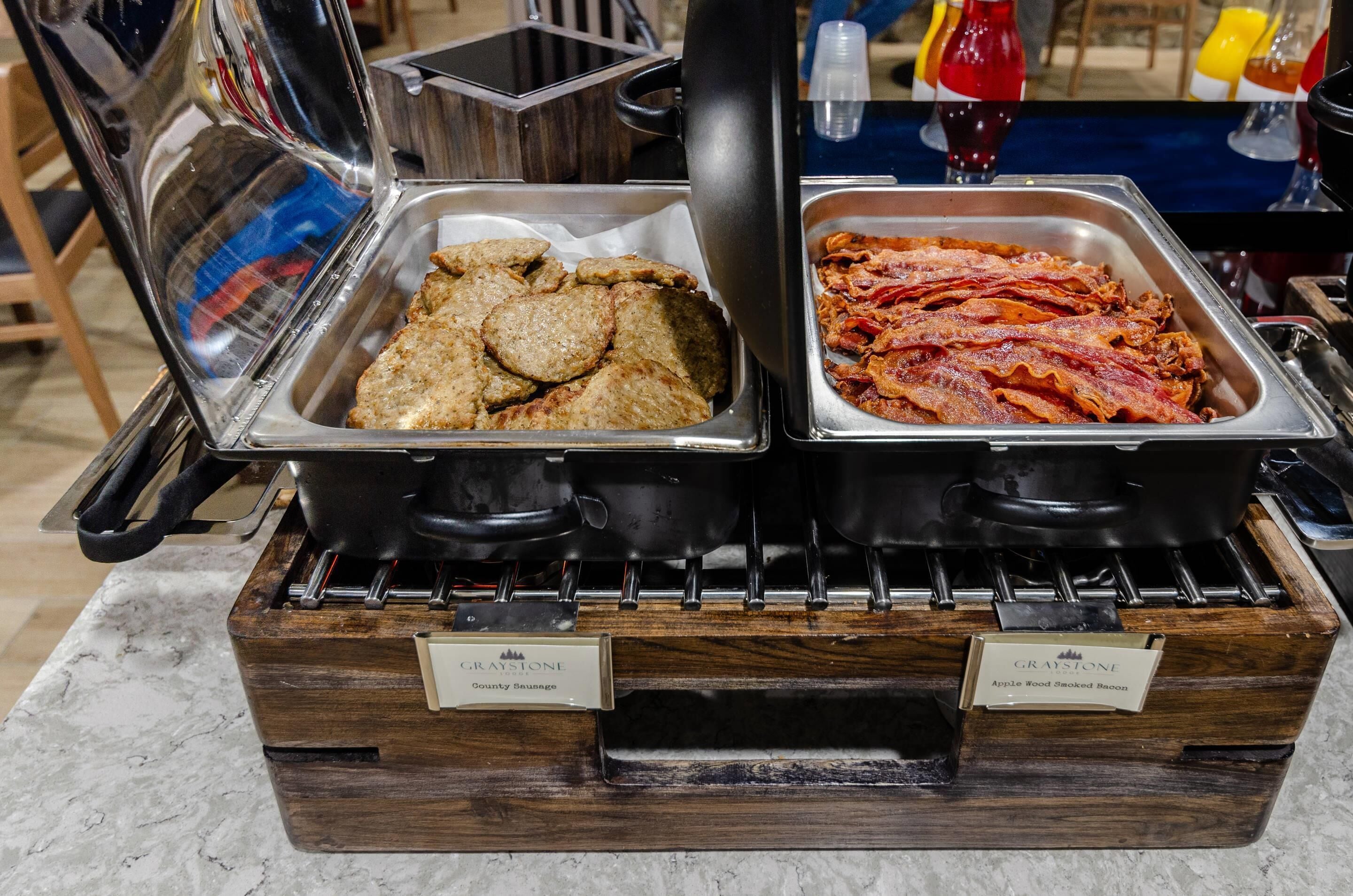 A buffet with two hot food stations, one labeled 'County Sausage' and the other 'Apple Wood Smoked Bacon'.