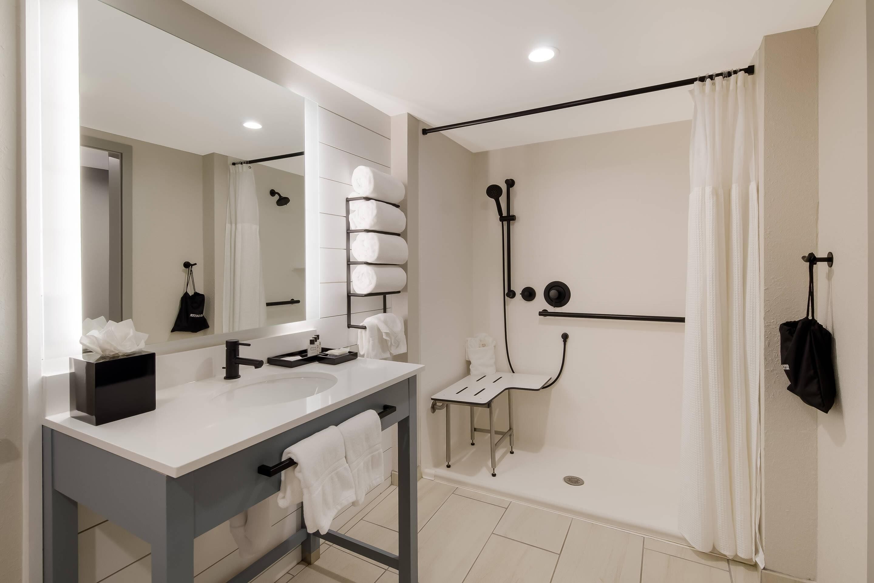 Une salle de bain moderne avec un meuble-lavabo à deux vasques, un grand miroir, une douche avec un tuyau noir et un porte-serviettes.