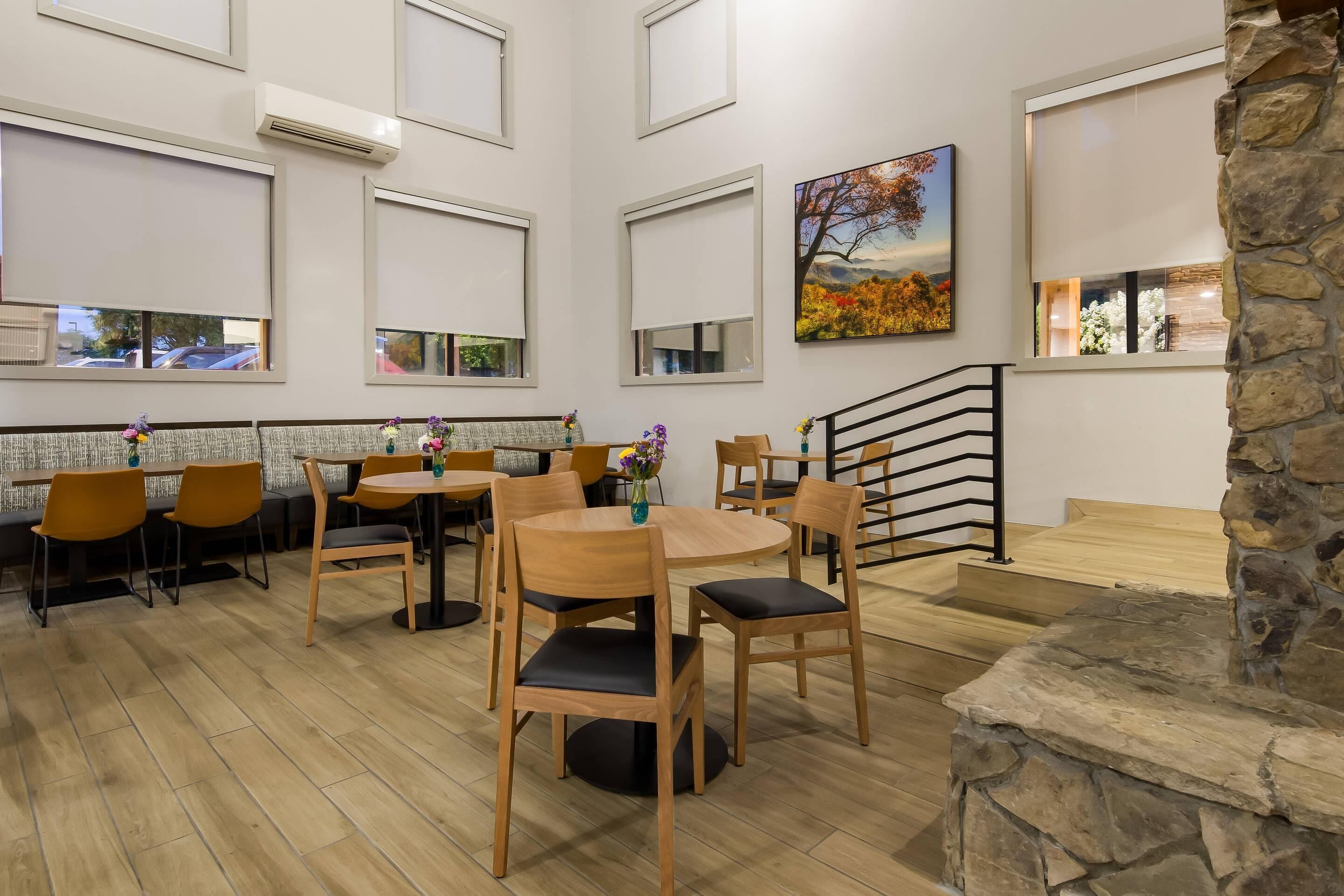 A restaurant with wooden tables and chairs, a stone fireplace, and a staircase.