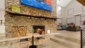 A stone fireplace with a fire, a dining table with chairs, and a modern living area with sofas and a staircase.