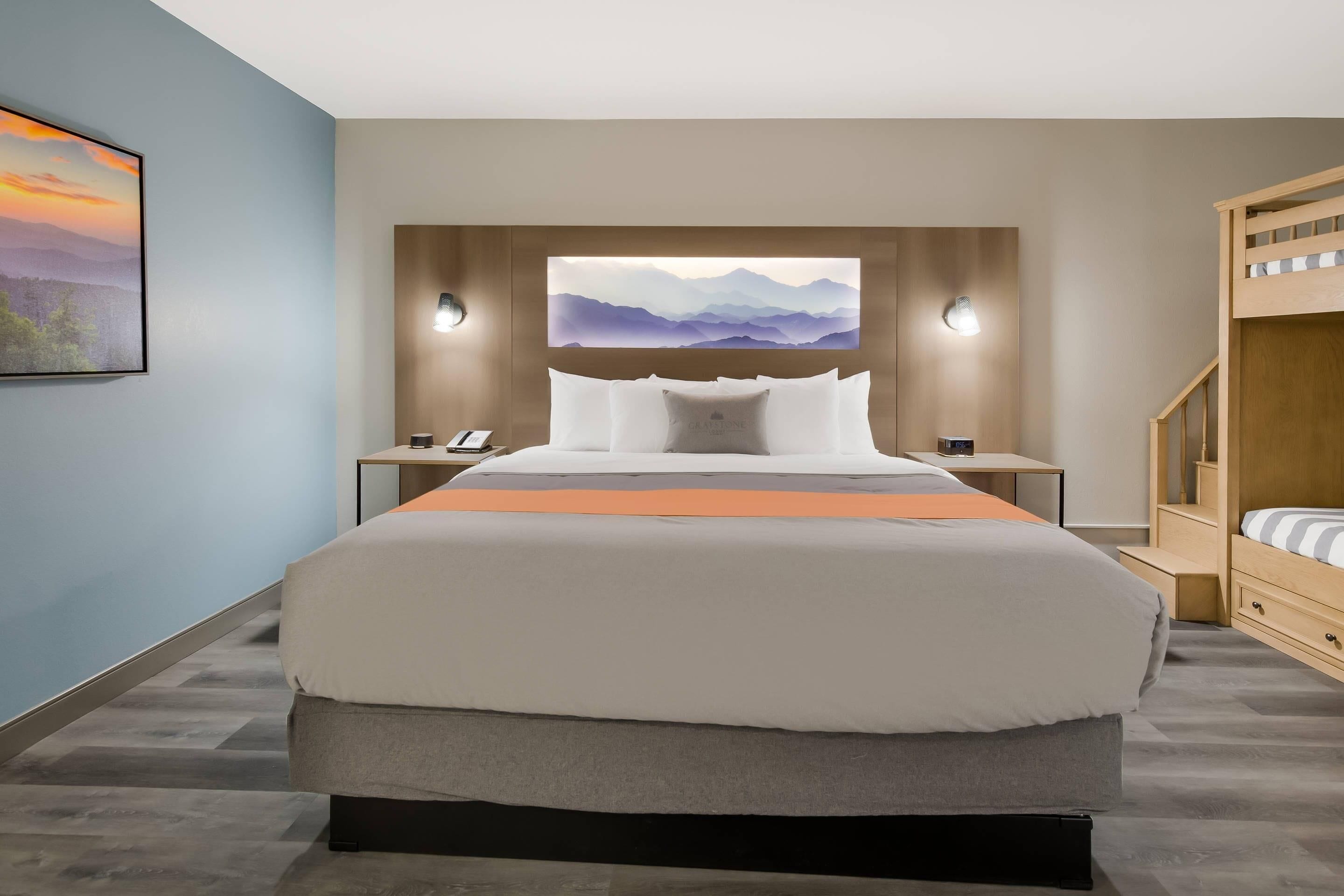 A modern hotel room with a large bed, a wooden bunk bed, a wall-mounted artwork, and a nightstand with a phone.