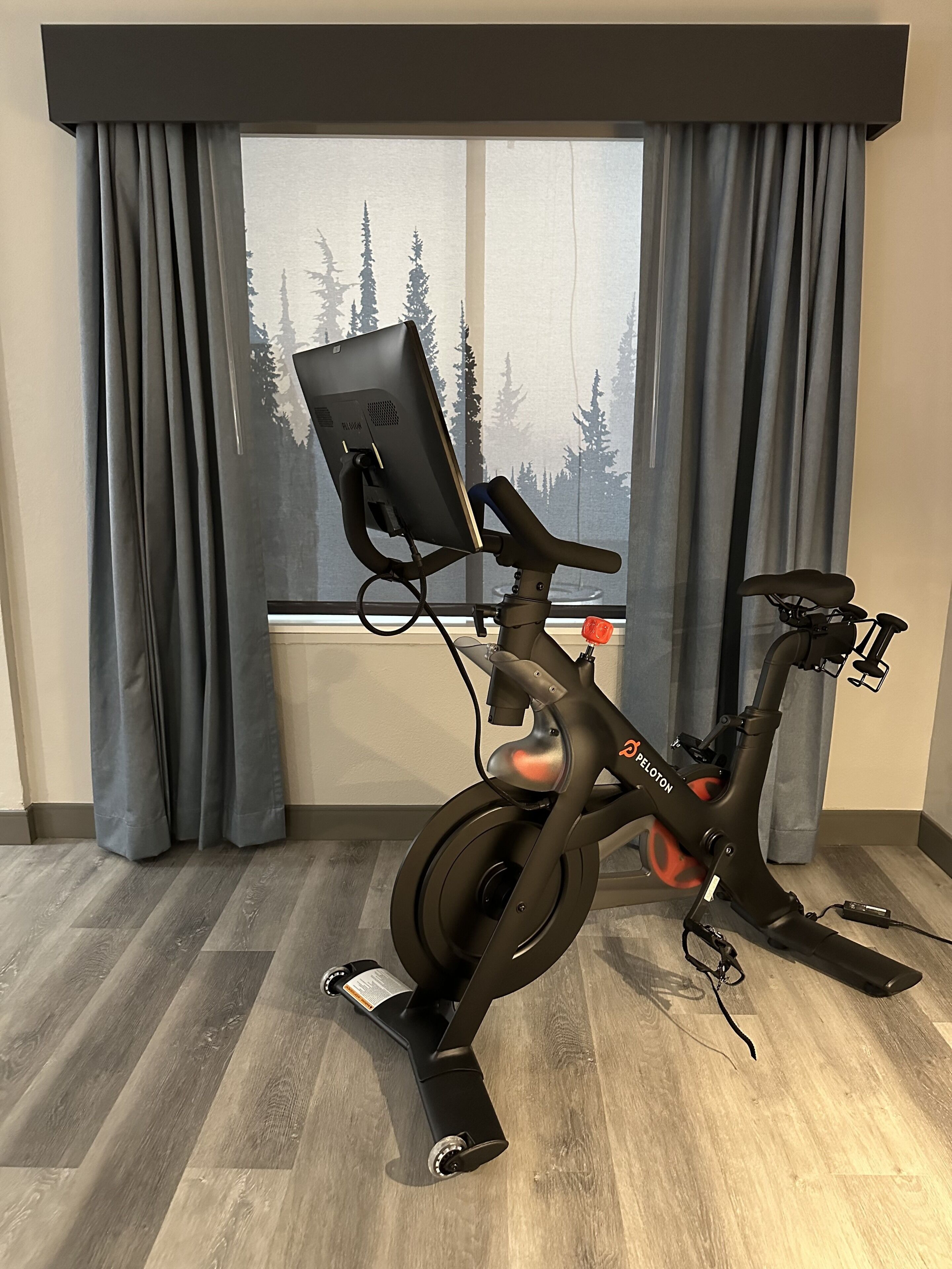 En stillesiddende motionscykel med skærm, pedaler og styr i et rum med et vindue og gardiner.