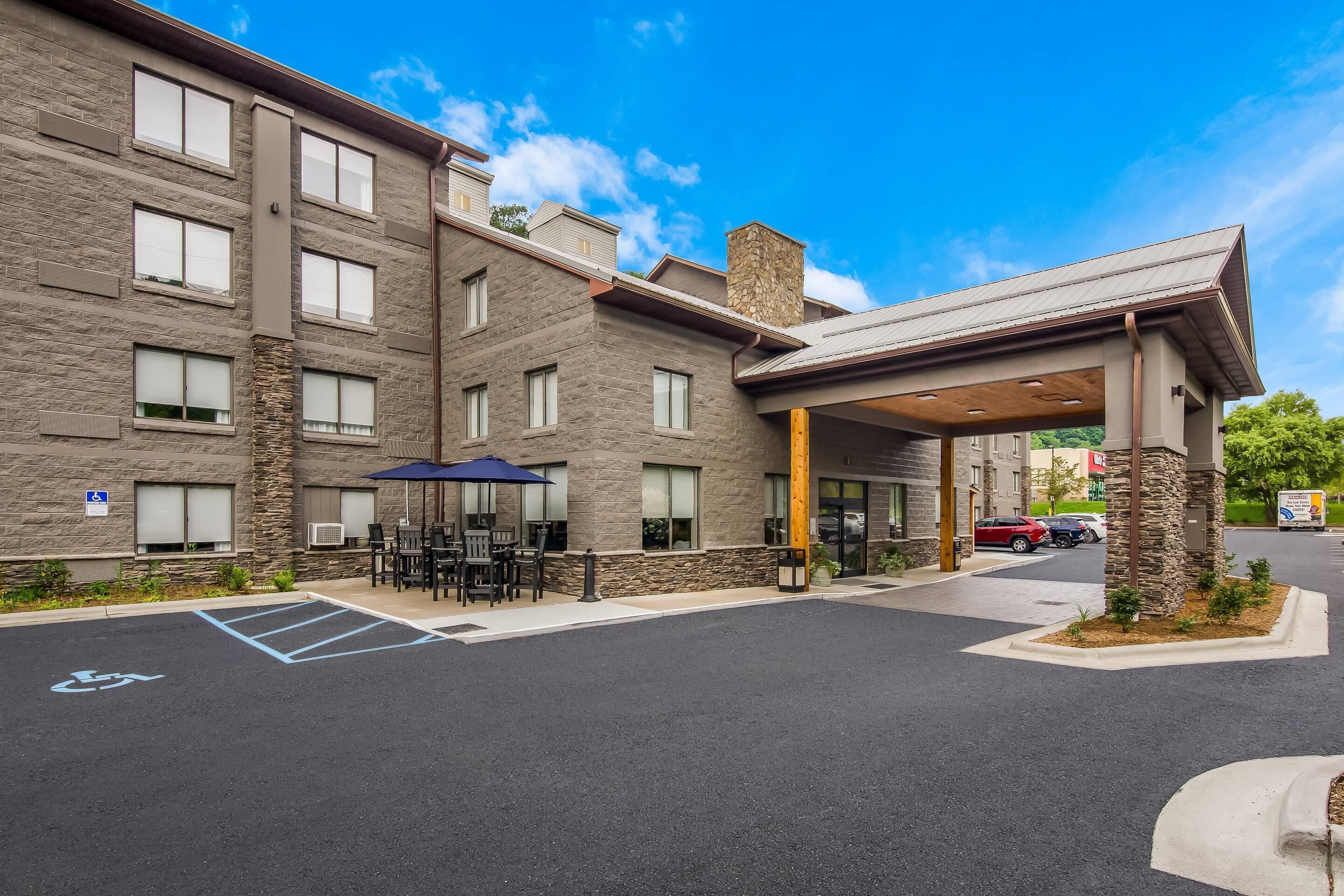 A multi-story hotel with a covered entrance, outdoor seating area, and a handicapped parking space.