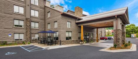 A multi-story hotel with a covered entrance, outdoor seating area, and a handicapped parking space.