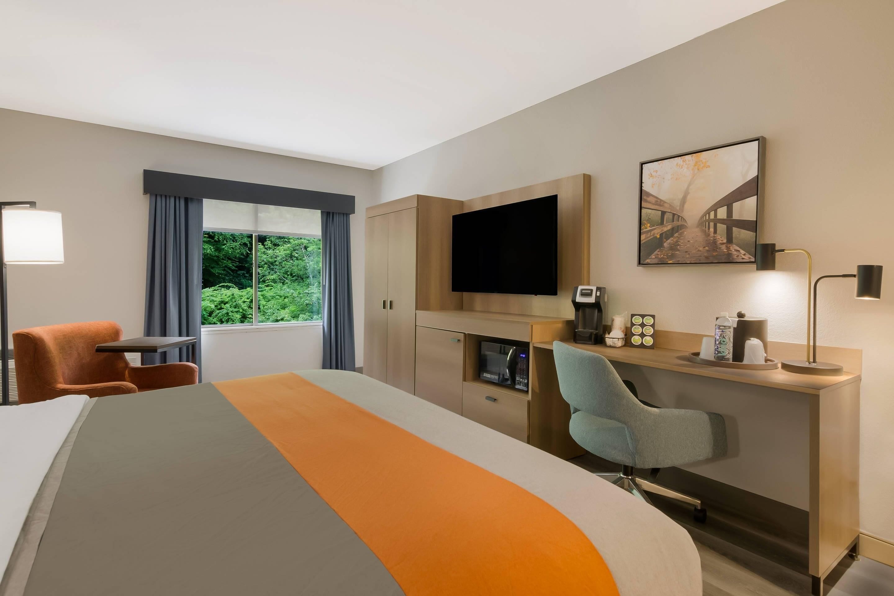A hotel room with a bed, a desk, a chair, a TV, and a window with curtains.