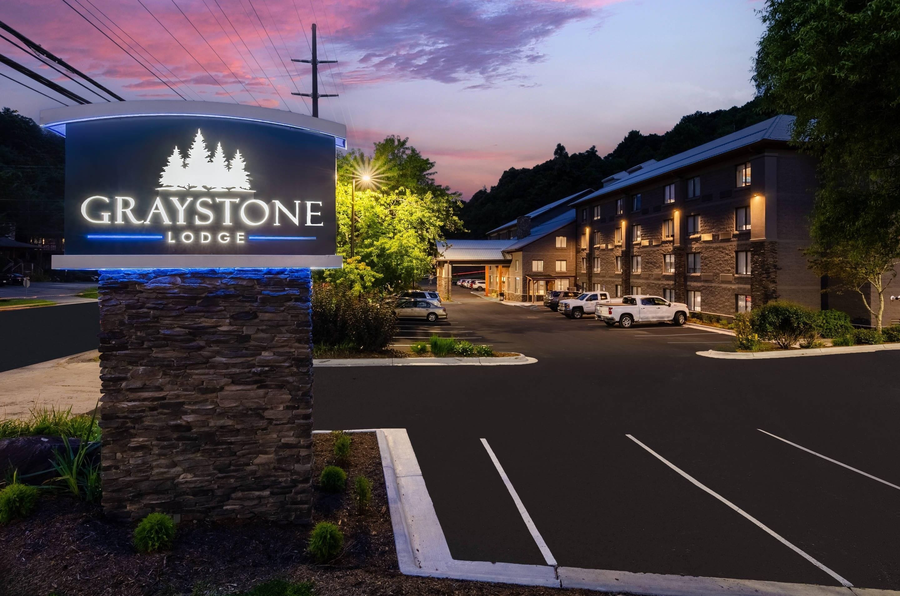 Een hotelingang met een bord waarop 'GRAYSTONE LODGE' staat en een parkeerplaats ervoor.