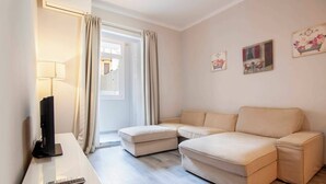 A modern living room with a beige sectional sofa, a flat-screen TV on a stand, and a remote control on a white table. - P2PAR1002- Super Bright & New 2B Apt in the center (Barcelona)