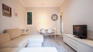 A modern living room with a sofa, a dining table with chairs, a TV, and a wall clock. - P2PAR1002- Super Bright & New 2B Apt in the center (Barcelona)
