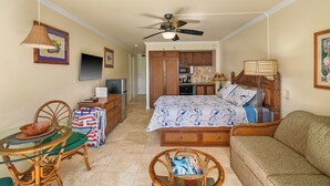 A compact room with a bed, a sofa, a dining table with chairs, a TV, and a ceiling fan.