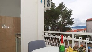 Ein Balkon mit einem Tisch, der für eine Mahlzeit gedeckt ist, einer Weinflasche und einem Obstkorb.