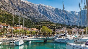 Ein Yachthafen mit vertäuten Booten, umgeben von einer gebirgigen Landschaft und Wohnhäusern.