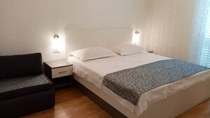 Ein ordentlich eingerichtetes Schlafzimmer mit einem Bett, Nachttischen und einem dunkel gefärbten Sofa.