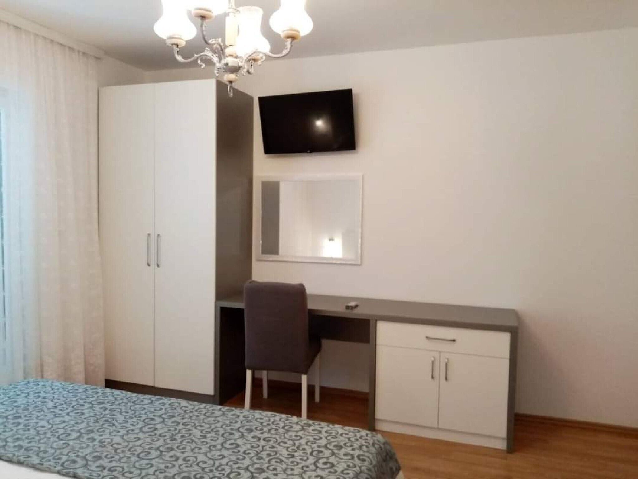 A bedroom with a bed, a desk, a chair, a television, and a wardrobe.