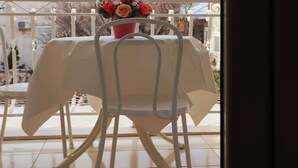 Ein Balkon mit Tisch, der mit einer weißen Tischdecke bedeckt ist, einem Stuhl und einem Blumentopf mit Blumen.