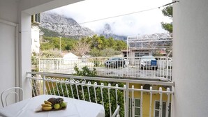 A balcony with a table set for dining, a view of a parking area, and a mountain in the background. - Apartments Pezo - Two Bedroom Apartment with Balcony (Baška Voda)
