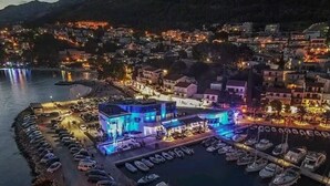 A waterfront hotel with a marina, featuring a modern building with blue lighting, a parking area, and boats docked. - Apartments Pezo - Two Bedroom Apartment with Balcony (Baška Voda)