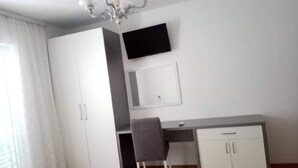 A bedroom with a bed, a desk, a chair, a wardrobe, and a TV on the wall.