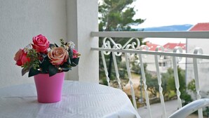 A pink flower vase on a white table on a balcony with a white railing and a view of buildings and trees in the background.