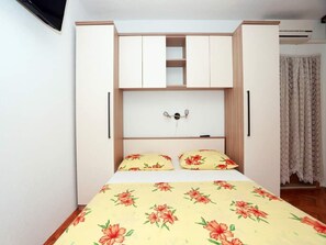 A bedroom with a bed, floral bedding, a wardrobe with multiple compartments, and a small shelf above the bed. - Apartments Pezo - Superior Two Bedroom Apartment with Balcony (Baška Voda)